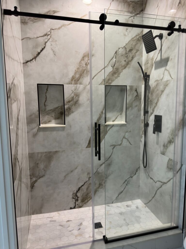 Bright bathroom with walk-in glass shower, marble-look tile, and black hardware