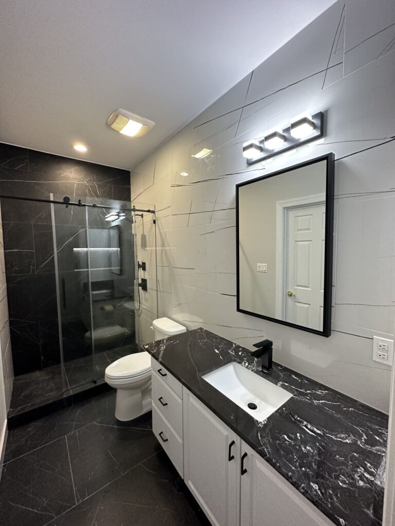 Black and white bathroom with walk-in glass shower, matte black fixtures, and dark vanity countertop