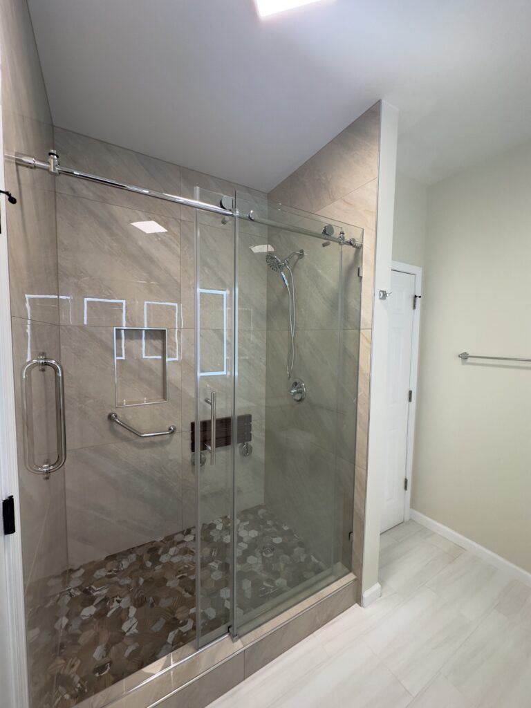 Bright bathroom with walk-in glass shower, double vanity, and illuminated mirrors
