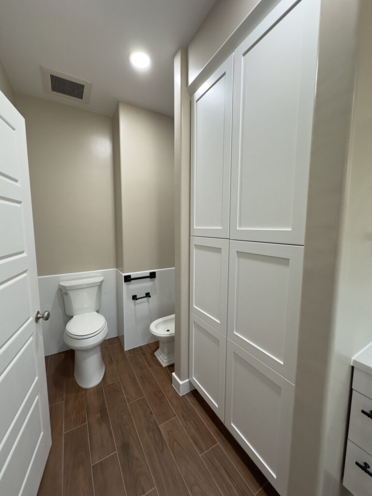 Modern bathroom remodel with clean white shower walls, black fixtures, and wood-look flooring