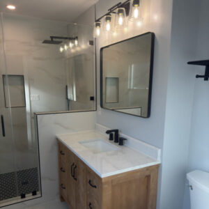 Bathroom remodel with walk-in glass shower, wood vanity, and black fixtures