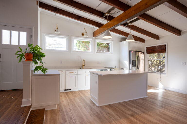 Bright kitchen with white cabinetry, large island, and exposed wood ceiling beams