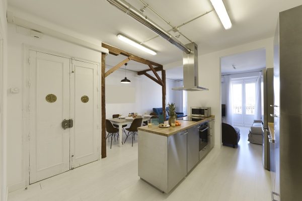 Open kitchen with stainless steel furniture, natural wood countertops and dining room with wooden table and brown upholstered chairs